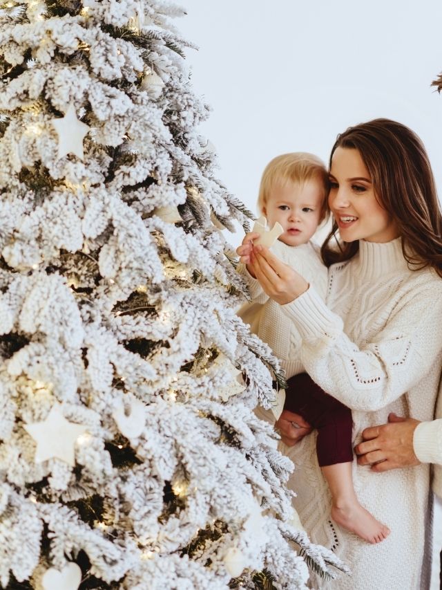 A family with a baby in front of a white christmas tree.