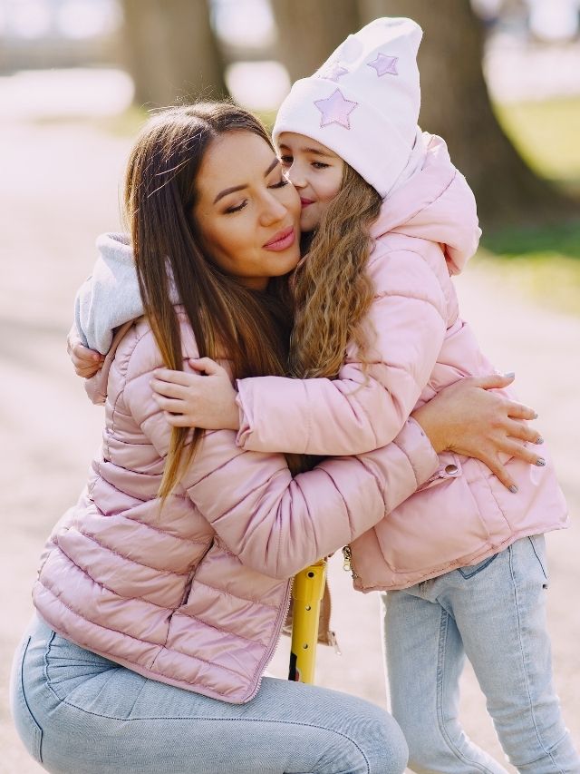 A mother and daughter hugging in the park.