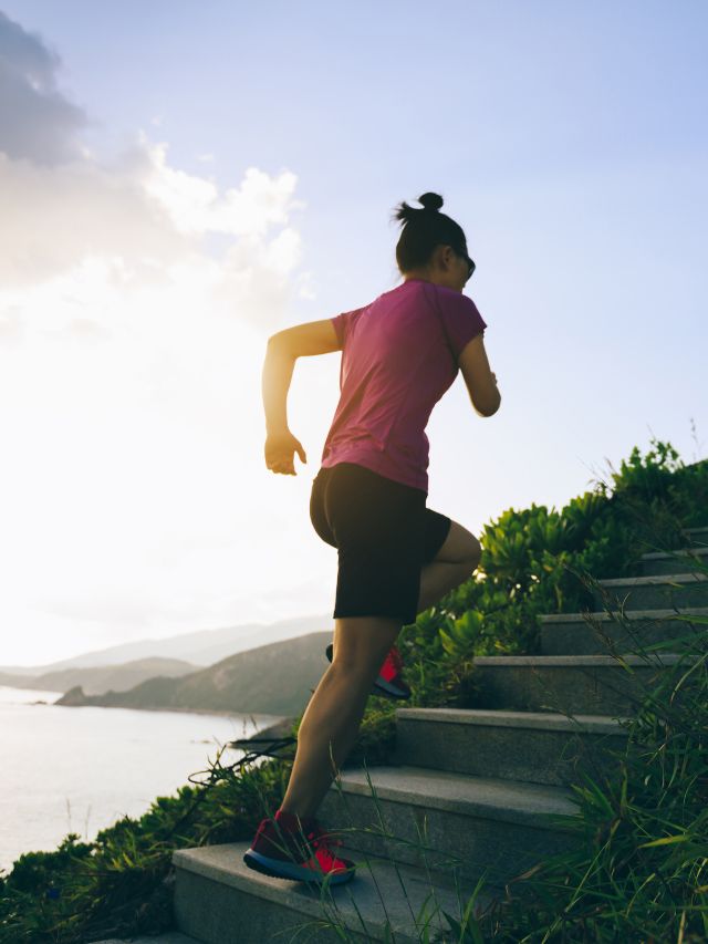 A woman jogging on stairs near the ocean.