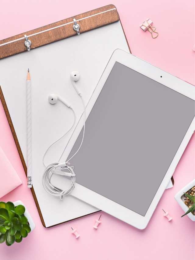 An ipad on a pink background with earphones and a notebook.