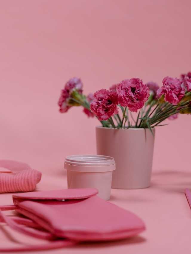 A pink vase with flowers and a pink purse on a pink background.