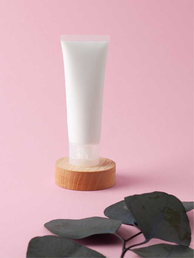A tube of cream on a wooden stand with eucalyptus leaves.