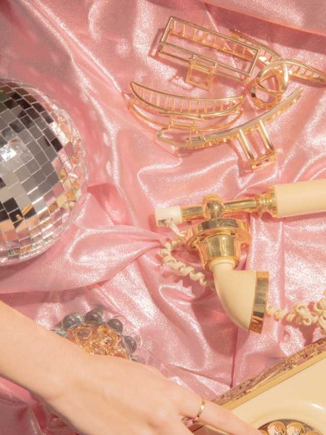A woman holding a gold disco phone on a pink cloth.