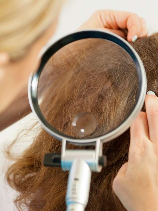 A woman is looking at her hair with a magnifying glass.