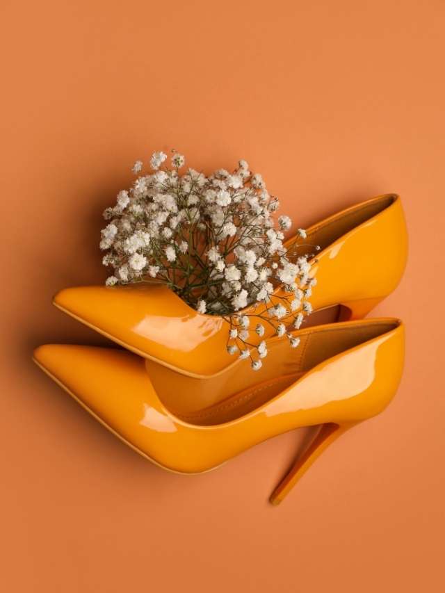 A pair of orange high heels with a bouquet of baby's breath on an orange background.
