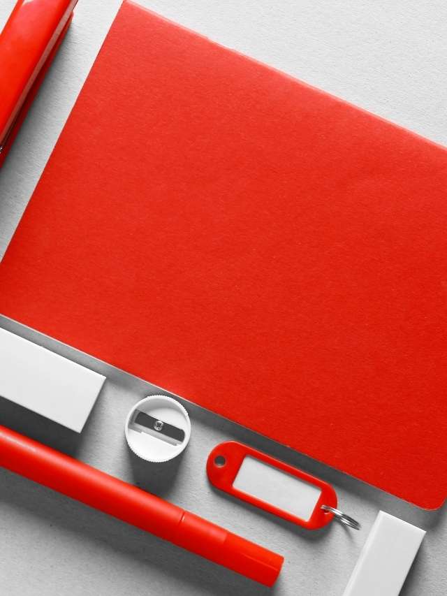 A red notebook, pens, and a pen laying on top of a white surface.