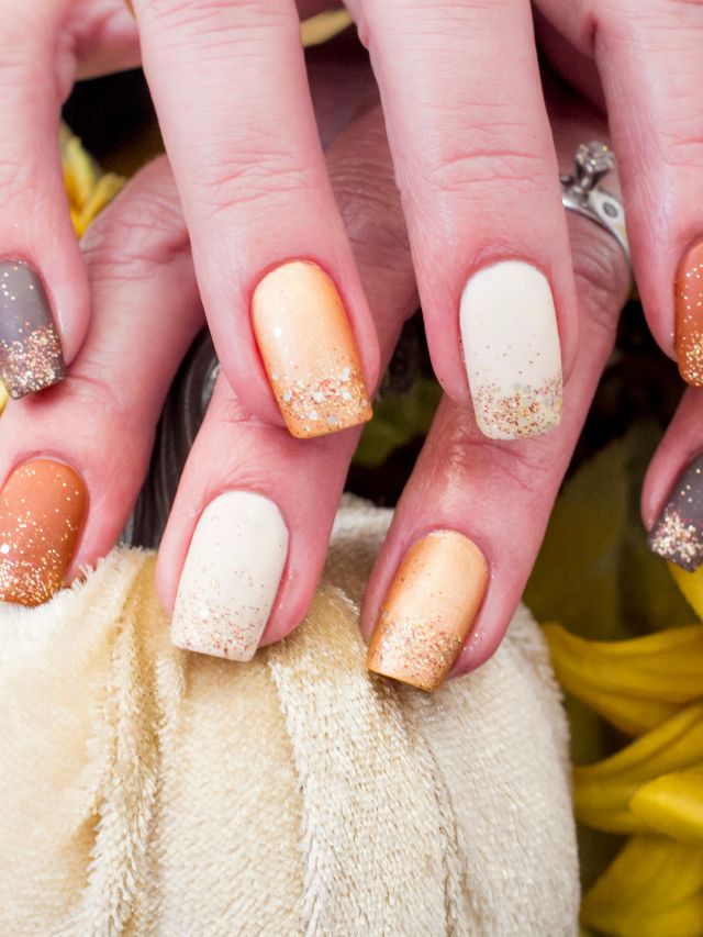 A woman's nails are decorated with gold and orange glitter.