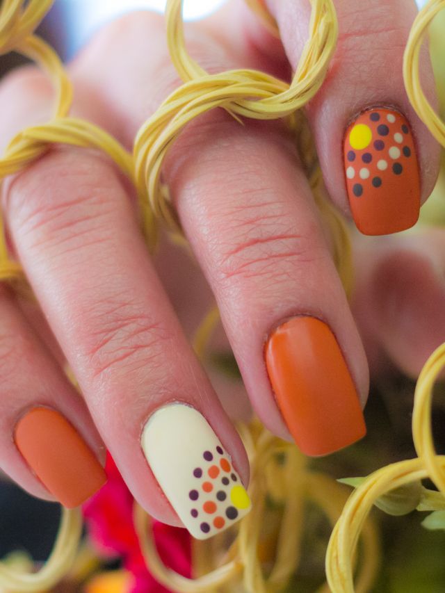 A woman's nails are decorated with orange and yellow polka dots.