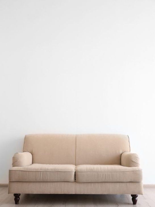 A beige couch against a white wall in an empty room.