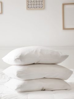 Three white pillows stacked on top of each other on a white bed.