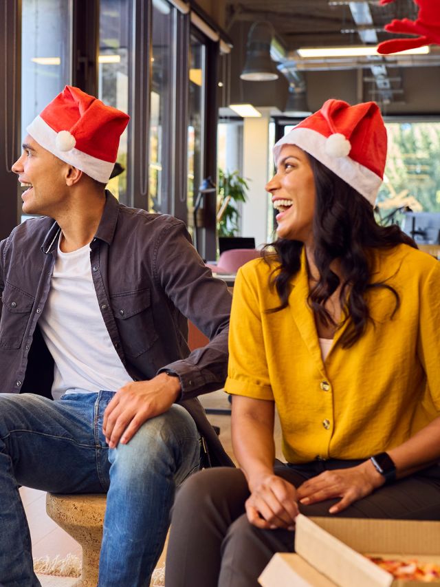 Two people in santa hats sitting in an office, celebrating Christmas.