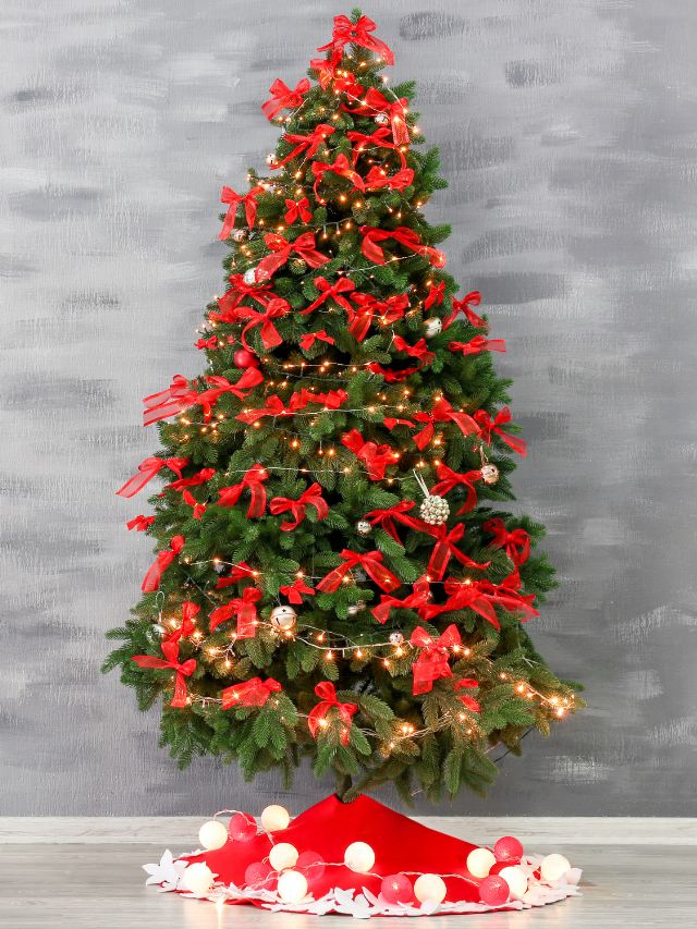 A christmas tree with red ribbons in front of a gray wall.