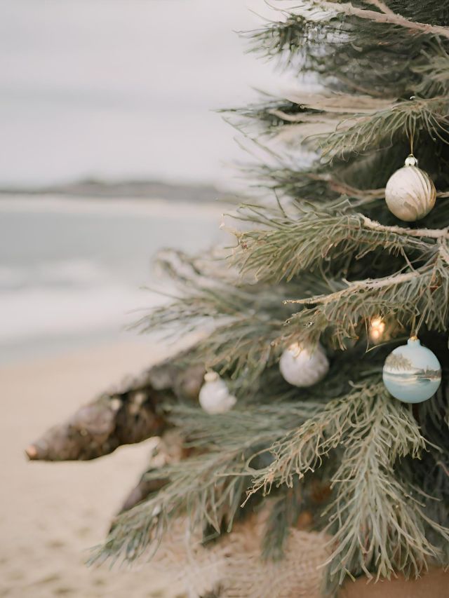 A christmas tree on the beach with ornaments.