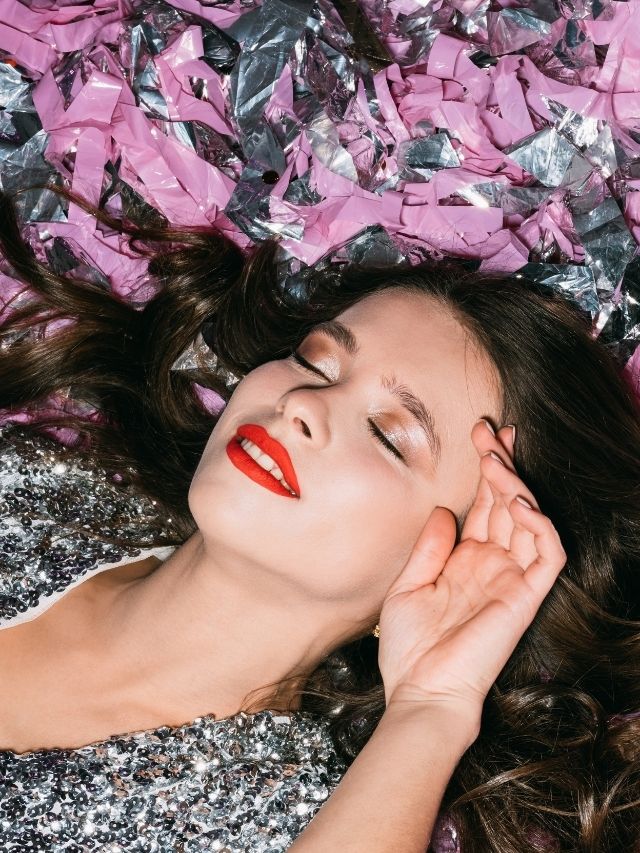A woman in a silver dress laying on confetti.
