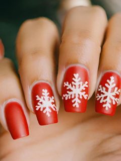 A woman is holding a cute red nail with white snowflakes, showcasing a festive Christmas nail idea.