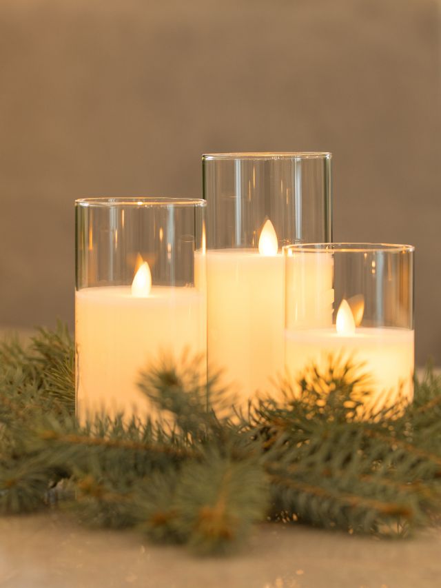 Three candles on a table with pine branches.