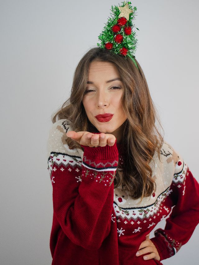 A woman wearing an ugly christmas sweater blowing a kiss.