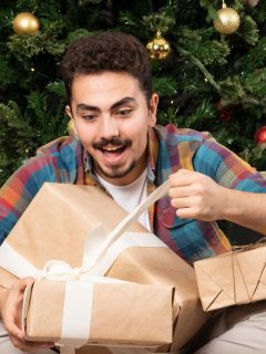 A man is opening a present in front of a christmas tree.