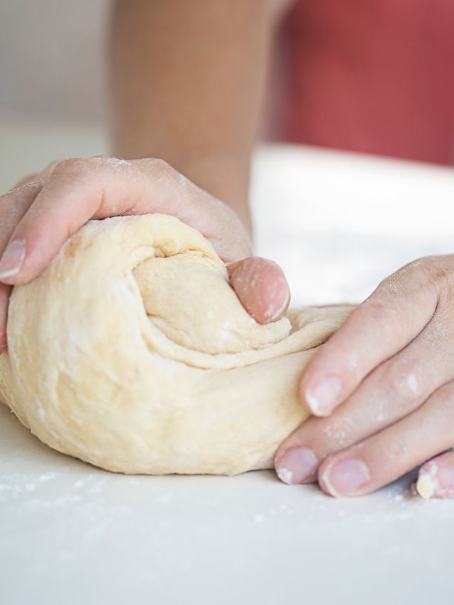 A person kneading dough on a white table.