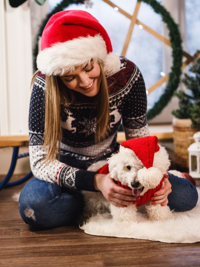 A woman wearing a santa hat with her white dog in a matching Christmas outfit.