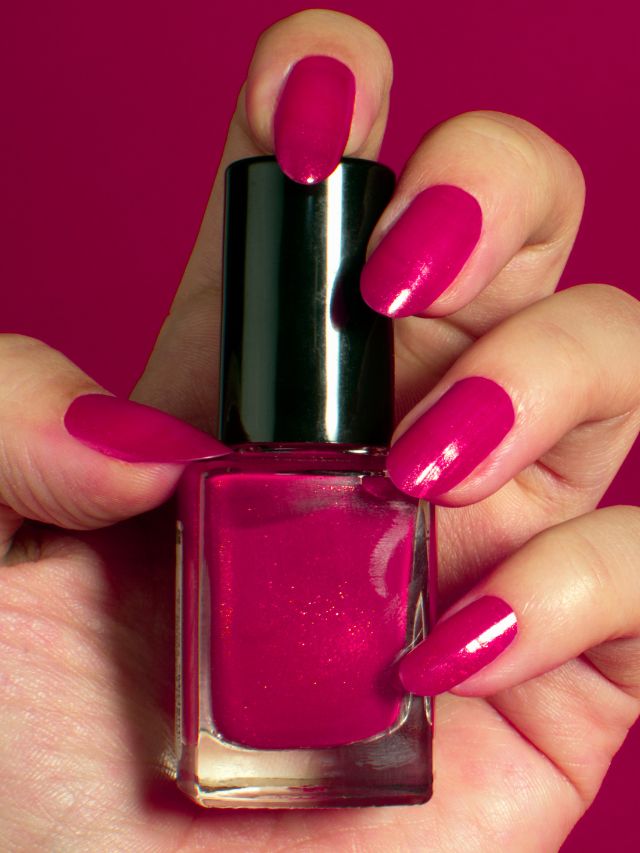 A woman's hand holding a pink nail polish bottle.