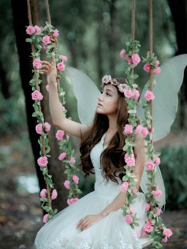 A girl in a fairy costume sitting on a swing.
