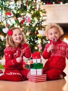 Two children sitting on the floor in front of a christmas tree.