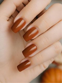 A woman's hand with brown nails and pumpkins.