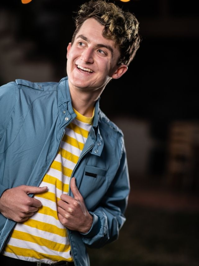 A young man wearing a striped shirt and jacket smiling for acting headshot.