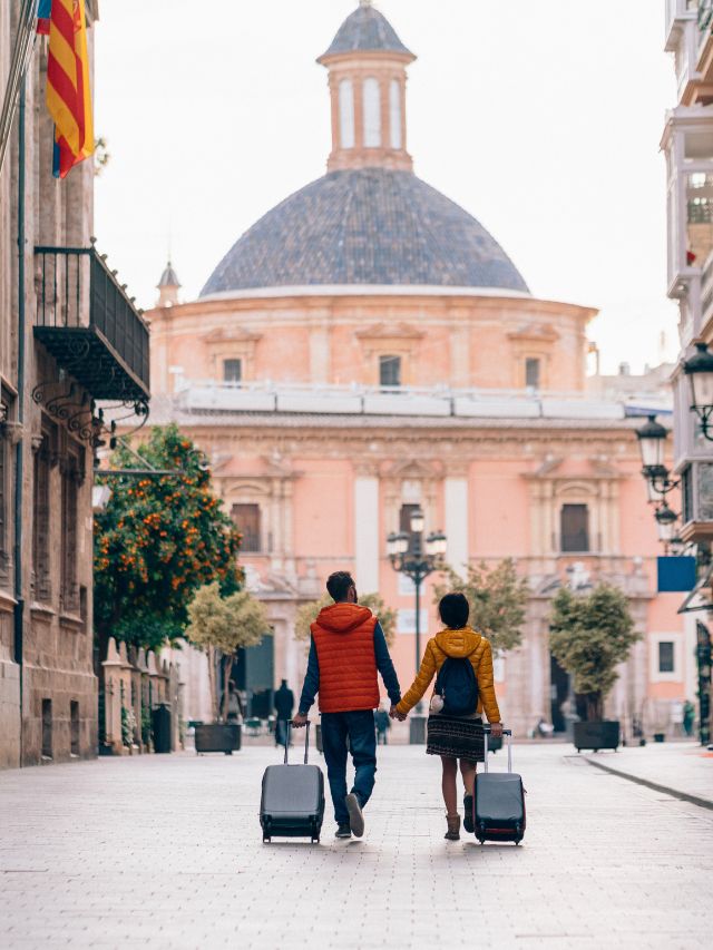 Two people walking down a street with luggage.