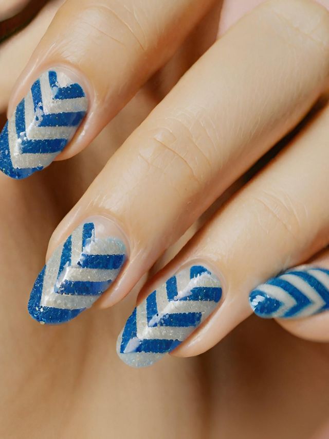 A woman's nails adorned with a chic chevron design featuring shades of blue and silver.