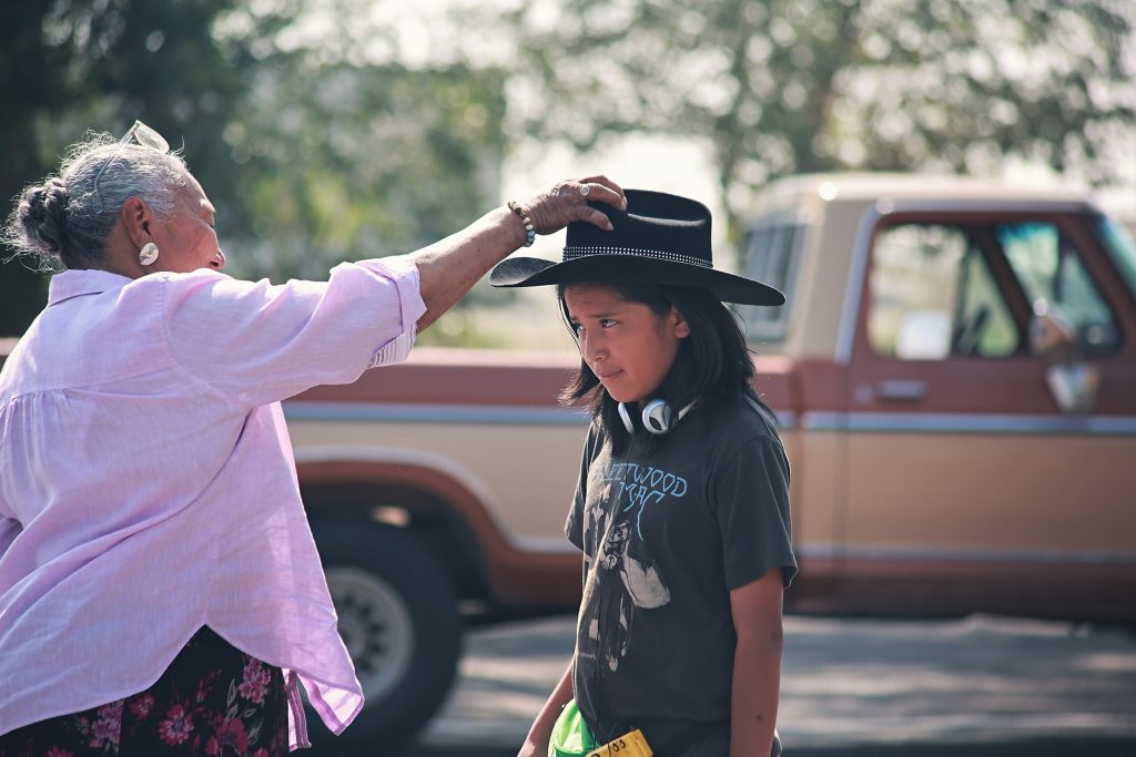 A woman is gently placing a boy's hat on his head.