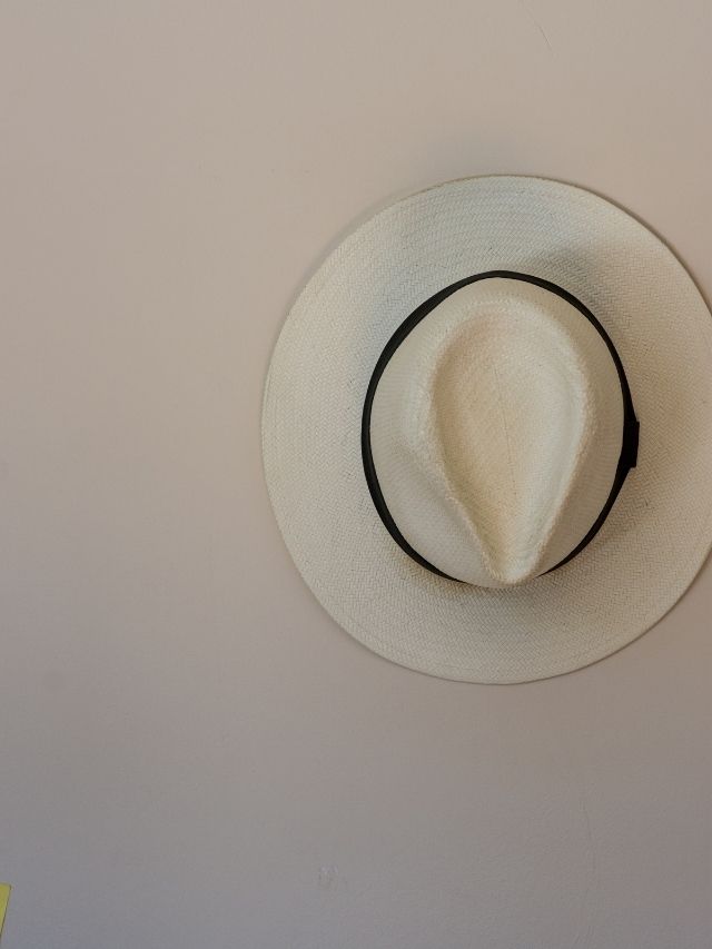 A white hat hanging on a white wall.