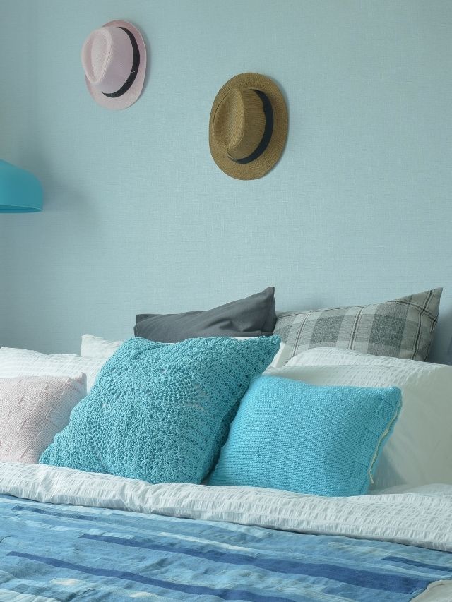 A bedroom with blue walls and a hat on the bed.