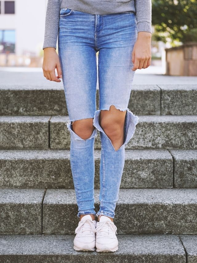 A woman wearing ripped jeans and a sweater standing on steps.
