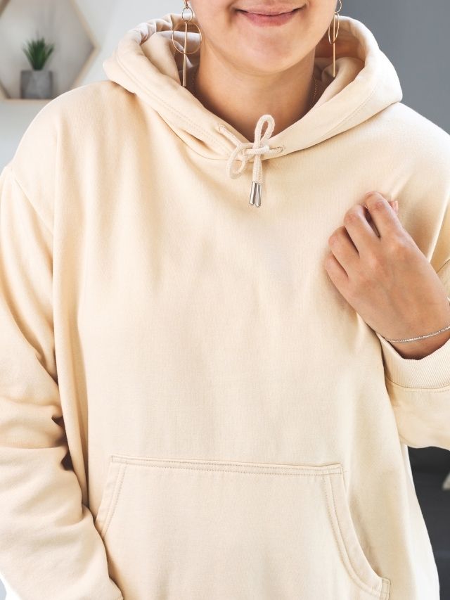 A woman wearing a beige hoodie posing for a photo.