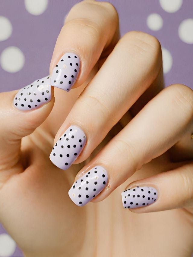 A woman's hand with purple and white polka dot nails.