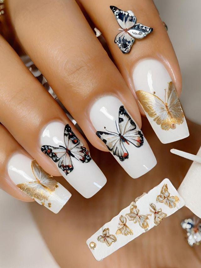 A woman is holding a white nail with gold butterflies on it.
