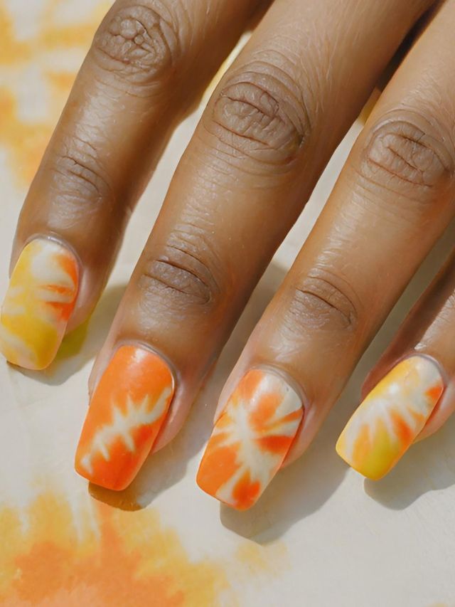 A woman's hands with orange and yellow tie dyed nails.