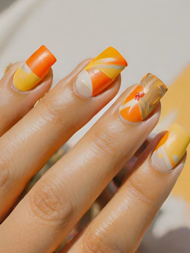 A woman's nails with orange and yellow designs.