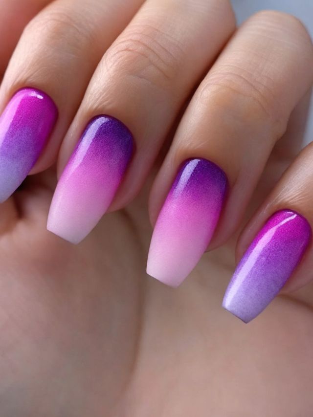 A woman's hand with stunning purple and pink ombre nails embellished with intricate nail art in shades of pink and purple.