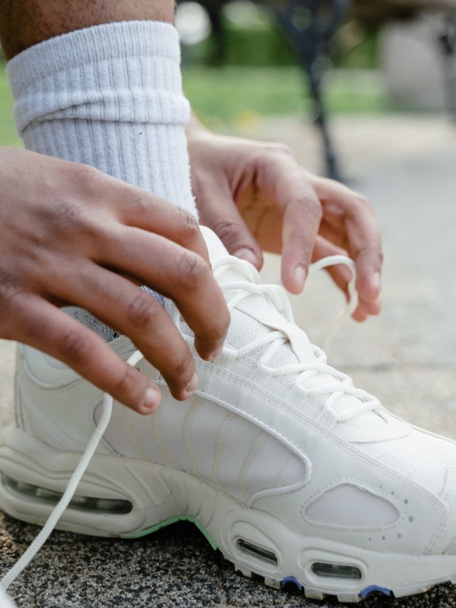 A man's feet tying a pair of white sneakers.