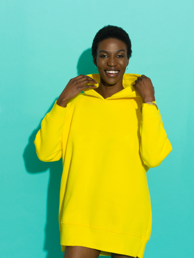 A young black woman in a yellow hoodie posing on a blue background.