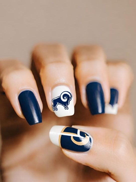 A woman holding up a nail with a rams logo on it.