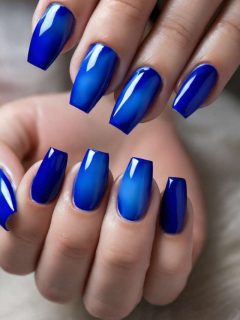 A woman with blue nails holding a blue nail polish.