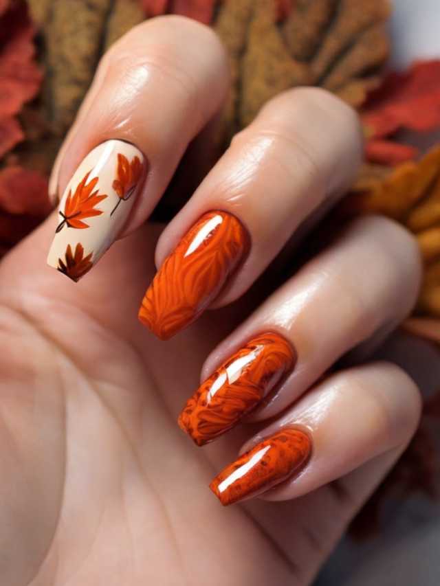A woman's hand with orange nails and leaves in the background.