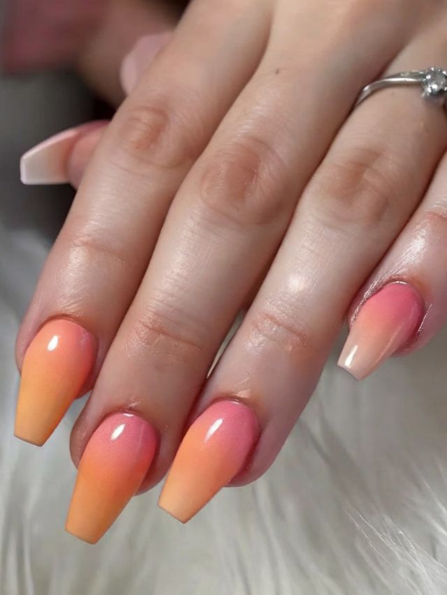 A woman's hand with orange and yellow ombre nails.