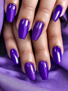 A woman's hand with purple nails on a purple fabric.