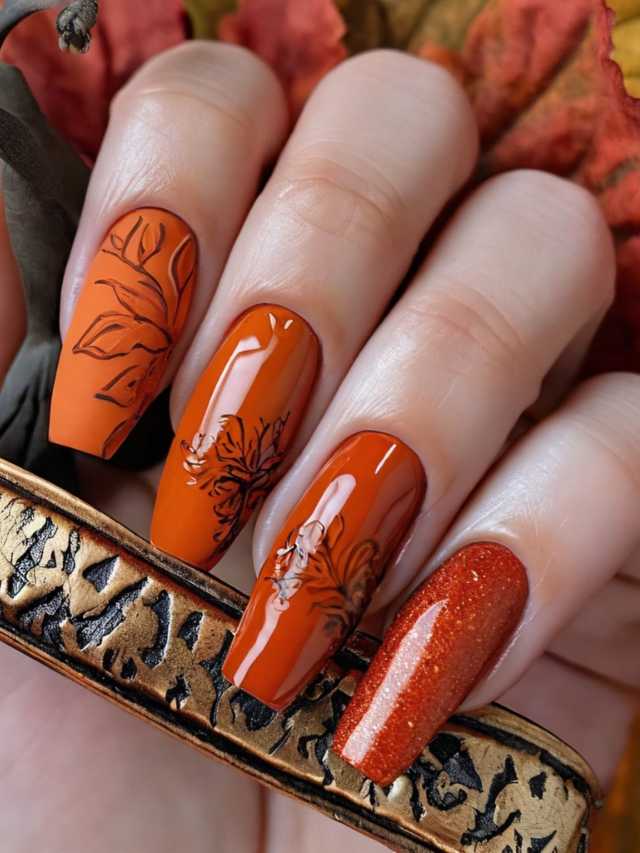 A woman's hand holding an orange nail with leaves on it.