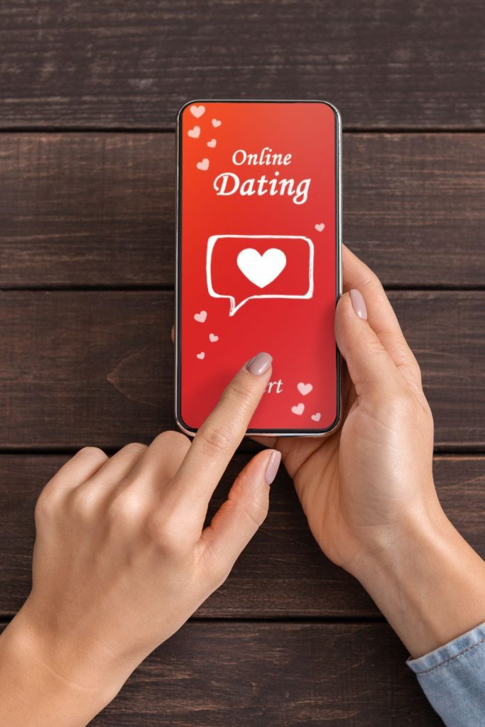 A woman holding a phone with the word online dating on it, searching for potential matches and crafting catchy dating profile headlines.